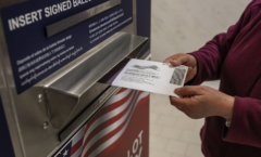 a person is inserting a mail in voting ballot into the USPS mail drop box