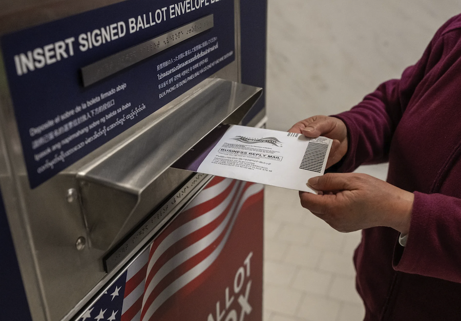a person is inserting a mail in voting ballot into the USPS mail drop box